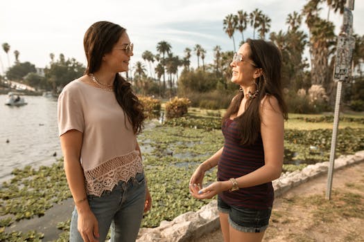 Two women having a casual conversation by a scenic lake on a sunny day.